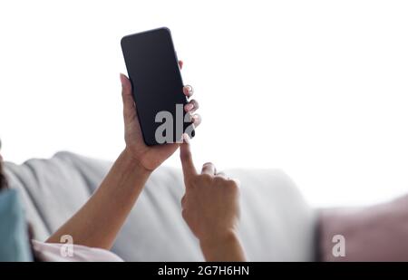 Contacter l'entreprise, la communication des personnes, l'appareil technologique. La femme afro-américaine millénaire se trouve sur un canapé en train de taper sur un smartphone avec un écran vide, wat Banque D'Images