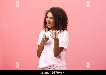 Hé, vous êtes génial. Enjouée charmante et heureuse, insouciante, cette jeune fille à la peau sombre et à la mode avec une coiffure en forme de boucles et un sourire qui fait bouger les doigts Banque D'Images