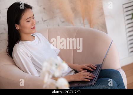 Portrait d'une femme asiatique appréciant l'utilisation d'un ordinateur portable à l'intérieur de l'appartement salon intérieur. Concept de flux de webinar de vlogger par appel vidéo Banque D'Images