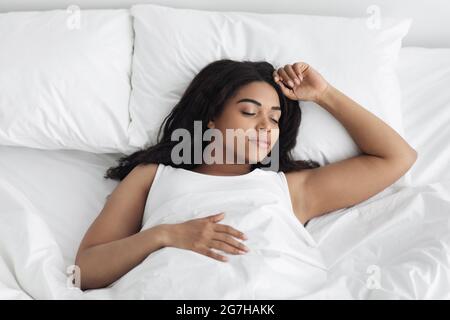 Coucher confortable. Jeune afro-américaine dormant dans un lit blanc à la maison, espace copie, vue de dessus. Une femme noire paisible qui fait une sieste, se reposant dans une chambre confortable Banque D'Images