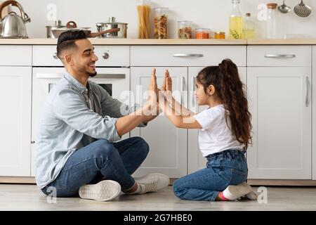 Beau père et fille de la famille du Moyen-Orient jouant dans la cuisine, assis sur le sol et se claquant les mains. Joyeux papa arabe et petite fille hé Banque D'Images