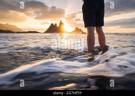 Partie basse de l'homme pendant la détente dans l'océan. Vue panoramique sur la plage de Benijo contre le ciel au beau coucher du soleil. Ténérife, Îles Canaries, Espagne. Banque D'Images