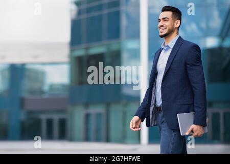 Un jeune homme d'affaires arabe heureux qui se promo depuis le bureau, tient un bloc-notes, regarde l'espace de copie et souriant, panorama. Un dirigeant musulman qui a réussi à prendre l'autobus Banque D'Images