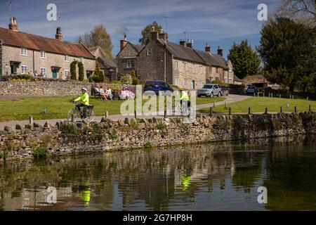 Royaume-Uni, Angleterre, Derbyshire, Tissington, The Green, cyclistes âgés en vestes haute viz, de l'autre côté de l'étang du village Banque D'Images