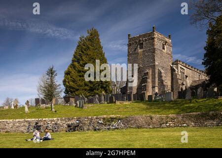 Royaume-Uni, Angleterre, Derbyshire, Tissington, cyclistes se reposant sur l'herbe sous l'église St Mary Banque D'Images