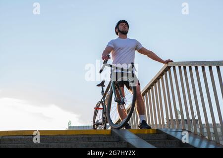 Homme sportif portant un casque de cyclisme, debout à l'extérieur de la ville avec son vélo Banque D'Images