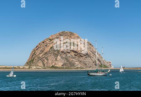 Morro Bay, CA, États-Unis - juin 10 2021 : gros plan de Brown Morro Rock dans l'océan Pacifique bleu profond sous le ciel bleu vu du centre-ville avec des bateaux sur la marina et p Banque D'Images