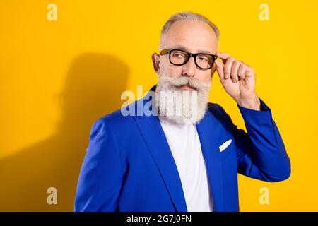 Photo de la barbe grise stricte homme aîné look vide espace porter lunettes blouson bleu isolé sur fond jaune vif Banque D'Images