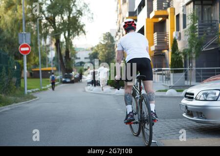 Vue arrière sur toute la longueur prise d'un homme à vélo dans la ville, portant un casque de vélo Banque D'Images