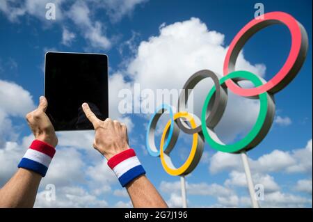 RIO DE JANEIRO - AVRIL 2016 : athlète portant un bracelet rouge, blanc et bleu touchant l'écran d'une tablette informatique devant les anneaux olympiques Banque D'Images