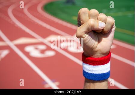 Un athlète avec un bracelet rouge, blanc et bleu pointe l'air devant un fond de piste de sport Banque D'Images