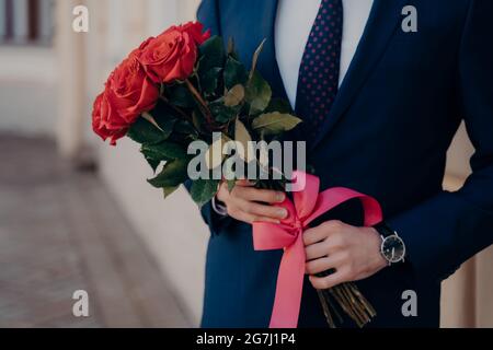 Homme vêtu d'un costume bleu portant un bouquet de roses rouges Banque D'Images