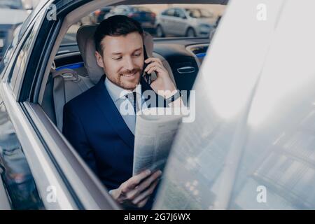 Un jeune cadre élégant en tenue formelle lit le journal sur le siège arrière de la voiture Banque D'Images