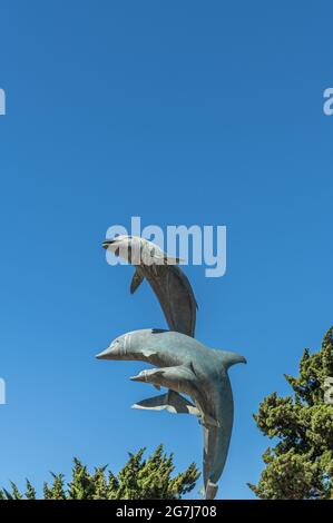 Cayucos, CA, Etats-Unis - 10 juin 2021 : gros plan des dauphins sautant sur la statue à la base de la jetée contre le ciel bleu. Banque D'Images