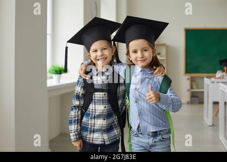 Portrait d'un petit étudiant joyeux en chapeau de graduation enserrant sourire à l'appareil photo Banque D'Images