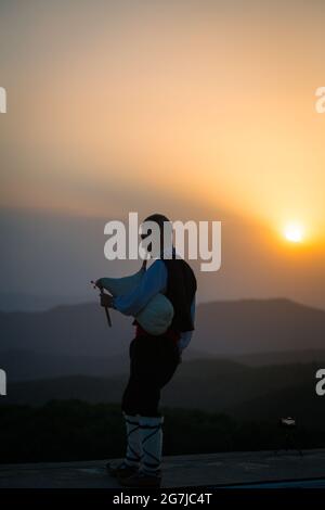 Un jeune joueur de cornemuse en costume folklorique joue sur un pic de montagne quand le soleil se lève, le matin 01 juillet 2021, Shipka, Bulgarie Banque D'Images