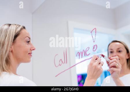 Inscription rouge à lèvres sur le miroir. La femme écrit les mots m'appellent. Banque D'Images