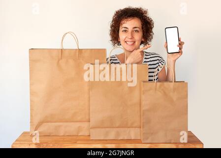 Une femme heureuse des achats faits par l'Internet points à son téléphone mobile à côté de quelques sacs d'achats Banque D'Images