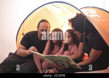 Belle vue d'une mère et d'un père avec deux filles lit un livre dans une tente Banque D'Images