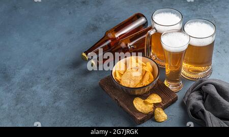 Trois tasses, chips et bouteilles de bière sur fond bleu foncé. Banque D'Images