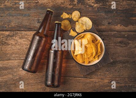 Des bouteilles de bière et des chips sombres dans un bol sur fond de bois. Banque D'Images