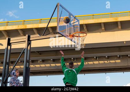 Kazan, Russie - 12 septembre 2020 : un jeune joueur de basket-ball jette une balle dans un panier de basket-ball contre le ciel bleu. Fond de panier en plastique transparent Banque D'Images