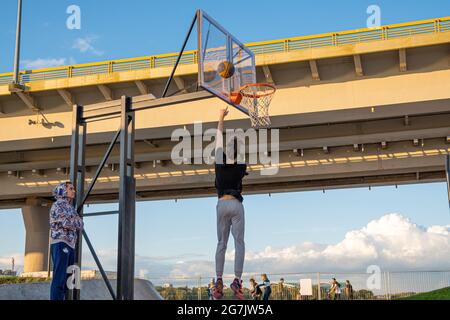 Kazan, Russie - 12 septembre 2020 : un jeune joueur de basket-ball jette une balle dans un panier de basket-ball contre le ciel bleu. Fond de panier en plastique transparent Banque D'Images