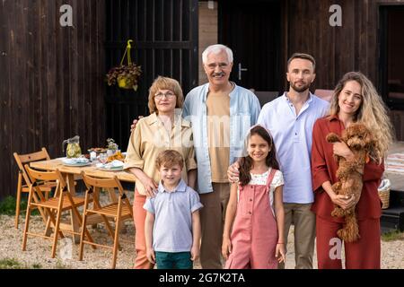 Portrait d'une grande famille heureuse avec parents, grands-parents, enfants et chien mignon debout aginst table de dîner Banque D'Images