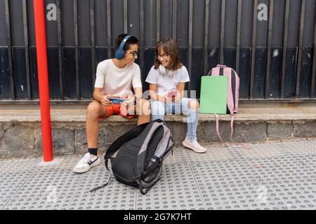 Des camarades de classe caucasiens attendent à l'arrêt de bus de l'école Banque D'Images