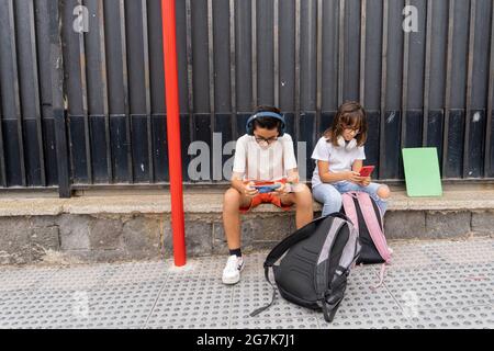 Des camarades de classe caucasiens attendent à l'arrêt de bus de l'école Banque D'Images