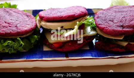 Incroyable nourriture de matière première colorée pour hamburger vegan de patate douce violette avec sauce tomate, salade, concombre, nourriture saine pour le petit déjeuner qui ri Banque D'Images