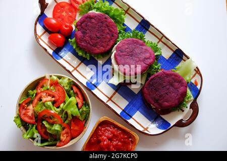 Incroyable nourriture de matière première colorée pour hamburger vegan de patate douce violette avec sauce tomate, salade, concombre, nourriture saine pour le petit déjeuner qui ri Banque D'Images