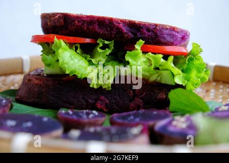 Délicieux hamburger végétalien de patate douce violette à la tomate, salade, nourriture saine pour le petit déjeuner que l'amidon riche, la fibre sur fond blanc Banque D'Images