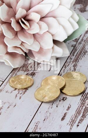 Petits jetons ronds en forme de bits dorés devant une grande fleur avec des pétales roses en arrière-plan et une surface en bois blanc Banque D'Images