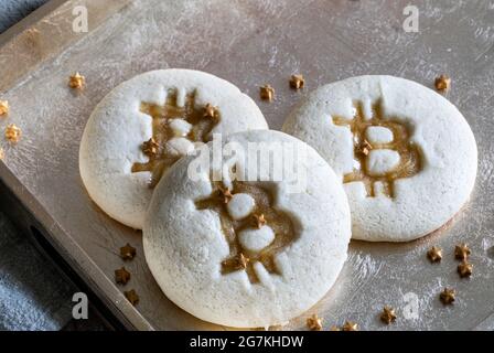 Biscuits de forme ronde avec le logo d'une célèbre pièce en forme de bit de curency crypto sur une surface dorée parsemée de lumière naturelle Banque D'Images