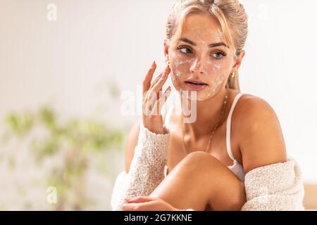 Gommage du visage appliqué par une jeune femme blonde dans sa maison. Banque D'Images