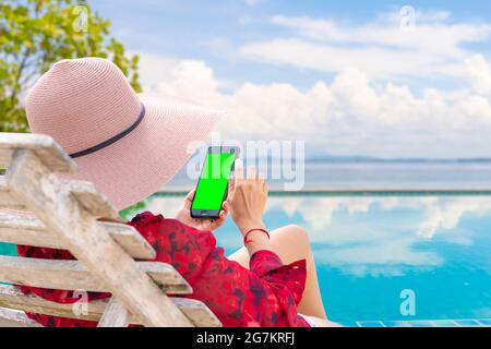 Femme utilisant un smartphone sur la piscine. Ses mains touchent l'écran vert du téléphone. Pour que les créateurs mettent des images supplémentaires. Banque D'Images