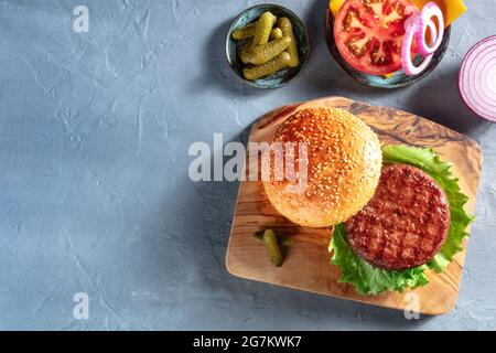 Ingrédients pour hamburgers. Patty hamburger, pain au sésame, m de tomate, oignon et cornichons, tiré du dessus sur fond bleu avec espace de copie. Recette de hamburger Banque D'Images