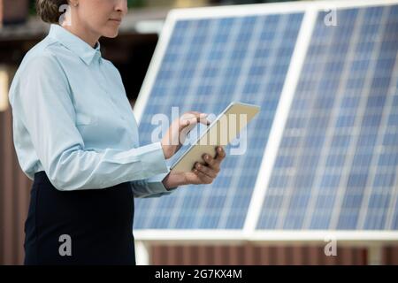Femme d'affaires travaillant sur un ordinateur tablette en se tenant contre des panneaux photovoltaïques sur la station d'énergie solaire Banque D'Images