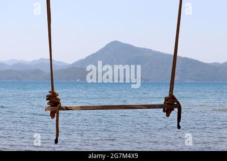 Balançoire en bois sur des cordes contre la mer bleue et les montagnes dans le brouillard. Vacances à la plage sur la station d'été Banque D'Images