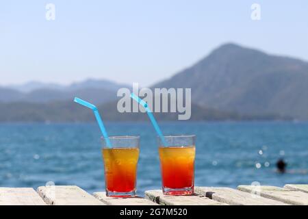 Deux verres avec cocktail sur une jetée en bois sur fond de mer et de montagnes. Vacances d'été sur une station balnéaire Banque D'Images