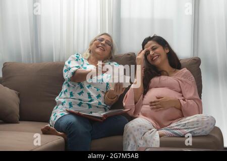 UNE FEMME ADULTE ÂGÉE ET UNE FILLE ENCEINTE RIENT AVEC DE VIEILLES PHOTOS Banque D'Images