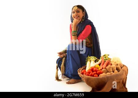 Une femme en costume de Giddha assise avec un panier de légumes à ses côtés. Banque D'Images