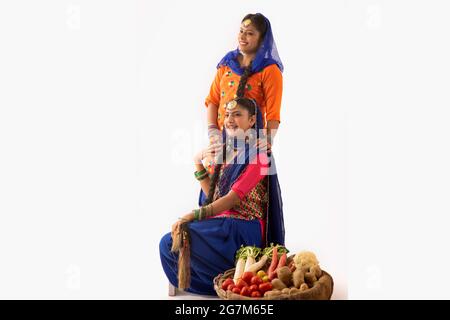 Deux femmes en costume de Giddha avec un panier de légumes à côté. Banque D'Images