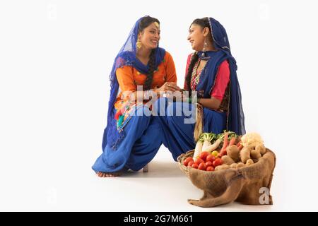 Deux femmes en costume de Giddha assis ensemble en tenant les mains avec un panier de légumes par leurs côtés. Banque D'Images