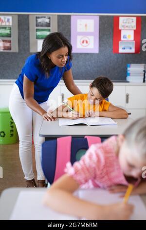 Une femme afro-américaine enseignant le garçon de race blanche en classe à l'école primaire Banque D'Images