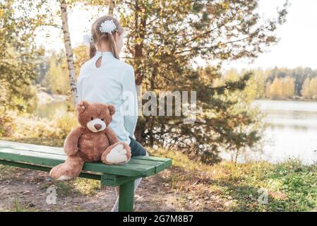 Une écolière aux noeuds et à l'ours en peluche regarde la rivière Banque D'Images