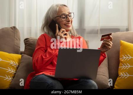 Une vieille femme parle au téléphone avec une carte à la main et un ordinateur portable sur les genoux. Banque D'Images