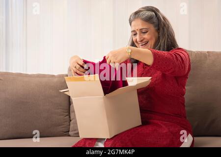 UNE FEMME ADULTE ÂGÉE SE FAIT UN PLAISIR D'OUVRIR UNE BOÎTE DE MESSAGERIE AVEC UNE ROBE Banque D'Images