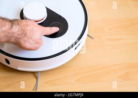 Homme allume manuellement un robot-aspirateur pour un nettoyage automatique de la pièce. Banque D'Images